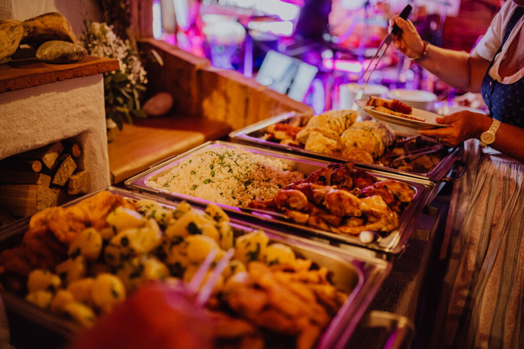 Gäste bedienen sich am warmen Buffet mit Braten, Knödeln, Reis und Kartoffeln