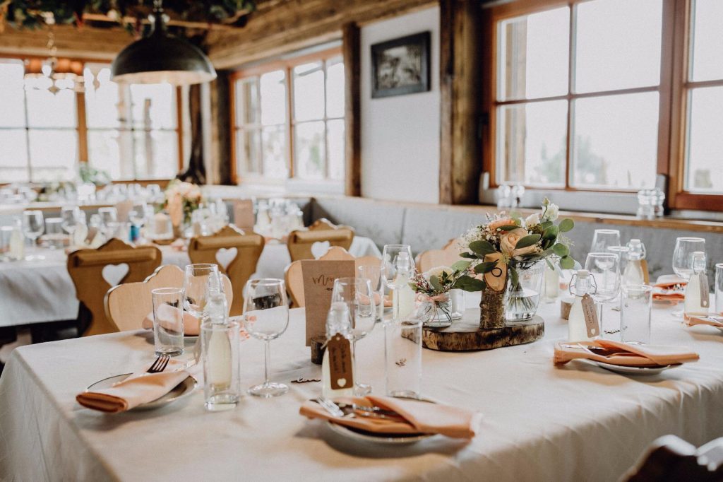 Hochzeitstische mit weißen Tischdecken, rosafarbenen Servietten und Blumen in der Holzstube